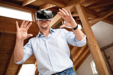 Mavi gömlekli erkek müteahhit, dairesinin sanal 3D gözlüklü uzantısına bakıyor ve şantiyede.