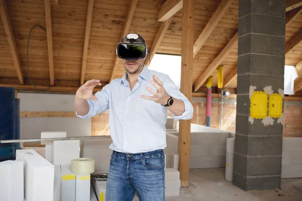 Male builder with blue shirt looks at the conversion, extension of his loft with virtual 3d glasses and is on the construction site