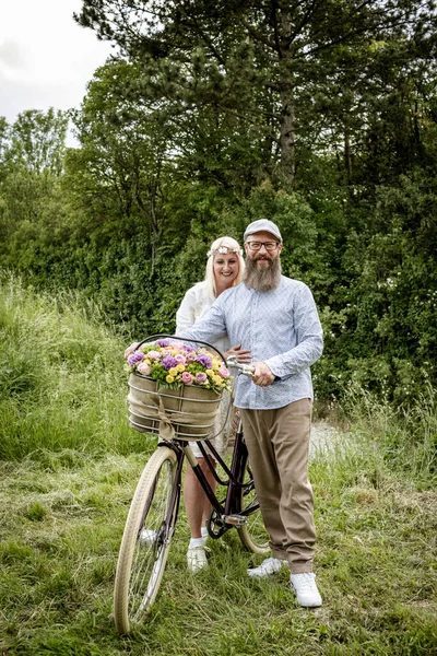 Blondynka Kobieta Białej Sukience Jej Mąż Pozowanie Rowerem Urządzone Kwiaty — Zdjęcie stockowe