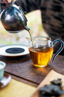 Doğanın bulanık arka planında çaydanlıktan bir fincana çay dökmek