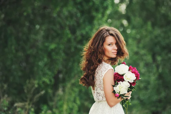 Novia feliz con un ramo de peonías en el árbol borroso de fondo . —  Fotos de Stock