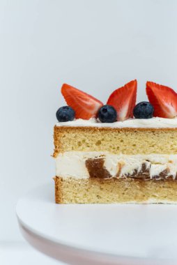 Krem peynirli pandispanya. Pasta yaban mersini ve çilekle süslenmiş. Beyaz izole arkaplan.