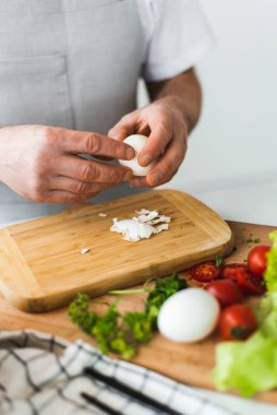 Bir adam kaynamış yumurtayı kesme tahtasına soyar. Sezar salatası pişiriyorum. Mutfakta yemek pişirmek. Yüksek kalite fotoğraf