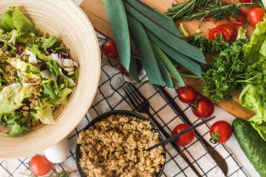 Salata için malzemeler rafta. Marul, pırasa, kinoa, maydanoz, domates. Yemek pişirme süreci. Mutfak masasında dağınıklık var. Yüksek kalite fotoğraf