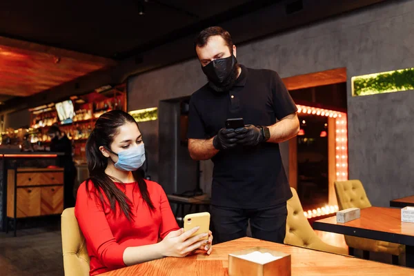 Social distancing during the covid-19 coronavirus pandemic. A restaurant visitor wearing a face mask making an order through the menu on the phone. Online menus help prevent the spread of infection.