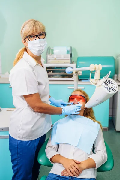 Teeth whitening. A patient in protective glasses from the rays in the chair at the dentist. Preventive examination of the oral cavity. Installing the mouth spacer. At the dentist appointment.