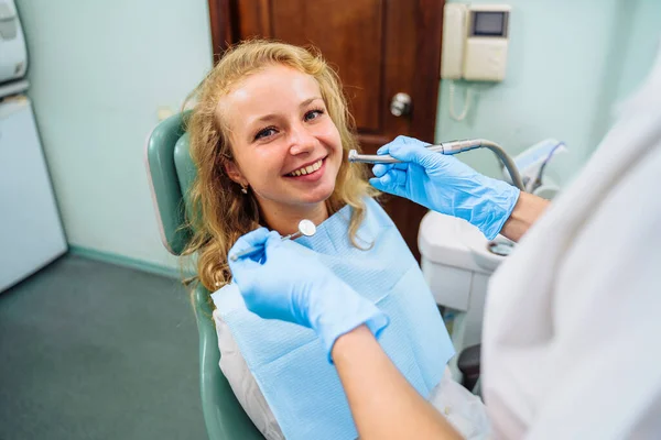 Dental treatment process. Drilling out problem areas of tooth and installing filling. Beautiful European patient sits in dentist\'s chair with an open mouth. Dentist holds medical instruments in hands.