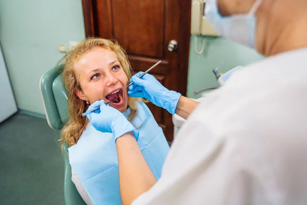 Dental treatment process. Drilling out problem areas of tooth and installing filling. Beautiful European patient sits in dentist\'s chair with an open mouth. Dentist holds medical instruments in hands.