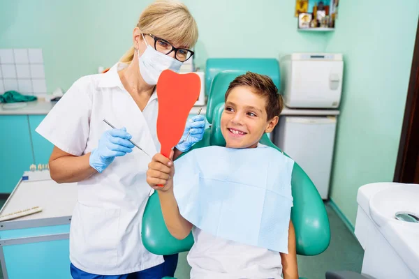 After dental treatment. The patient looks at healthy, snow-white, radiant smile after dental procedures. Tooth-shaped mirror. Satisfied with the result of going to the clinic.