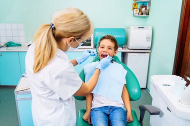 Modern bir klinikte dişçi randevusunda ağzı açık olan küçük bir hasta. Hastanede gülümseyen sevimli çocuk için muayene prosedürü yapan tanınmamış çocuk dişçisinin elleri..