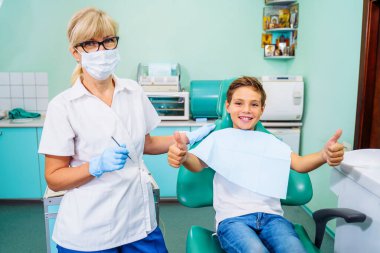 Küçük sabırlı çocuk dişçiye gittiği için mutlu. Acısız diş tedavisi kavramı. Güzel, geniş bir gülümseme bir doktorun muayenehanesinde dişçi koltuğunda oturan bir çocuk. Başparmaklar yukarı..