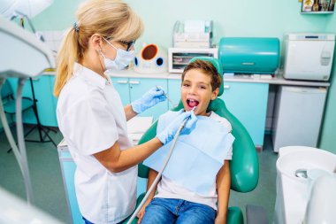 Modern bir klinikte dişçi randevusunda ağzı açık olan küçük bir hasta. Hastanede gülümseyen sevimli çocuk için muayene prosedürü yapan tanınmamış çocuk dişçisinin elleri..