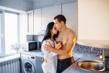 Sevgililer Günü 'nü kutluyoruz. Güzel çıplak figürleri ve vücutları olan heteroseksüel bir çift mutfakta sarılıp öpüşüyor. Elinde şarap kadehi tutan kız, tutkulu anın tadını çıkarıyor..