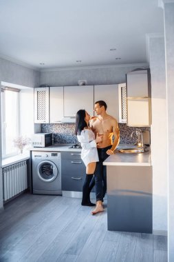 Sevgililer Günü 'nü kutluyoruz. Güzel çıplak figürleri ve vücutları olan heteroseksüel bir çift mutfakta sarılıp öpüşüyor. Elinde şarap kadehi tutan kız, tutkulu anın tadını çıkarıyor..