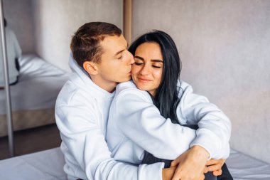 Aynı beyaz kapüşonlu ve siyah pantolonlu güzel genç çift yatakta sarılıyor. Birlikte mutlu bir gelecek düşlüyoruz. Birbirimizin arkadaşlığından zevk alıyoruz. # Adam nazikçe sarılır sevgilisine arkadan #.