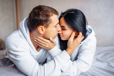 Sevimli, çekici, çekici Avrupalı genç erkek ve kadın yatakta rahatça uzanıyorlar. Pencereden dışarı bakıp, sarılıp, birbirimizi okşayacağız. Alınları, yüzleri, öpüşmeleri. Evdeki şefkat.