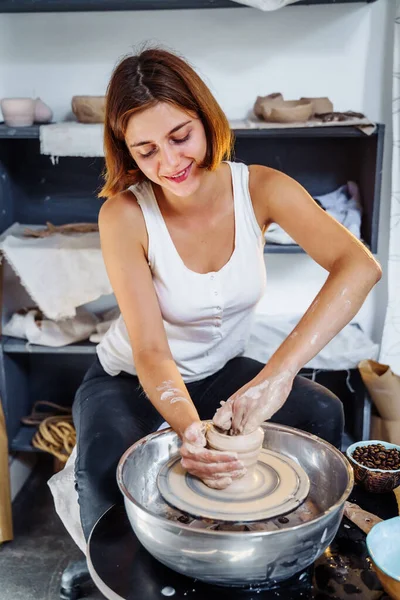 Potter woman, sculptor, with a sculpting tool, creatively shapes a piece of wet clay with a potter\'s wheel. Professional workshop for DIY work, handmade workshop for pottery. Hands making clay pot.
