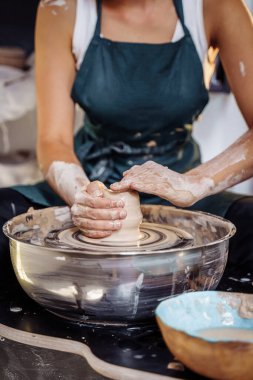 Profesyonel el hareketleriyle, bir kadın çömlekçi çömlekçinin tekerinde bir parça kil hazırlar, killeri yoğurur ve bir kase, vazo, sürahi, tabak yapmak için yuvarlar. Çömlek stüdyosu. Genç profesyonel.