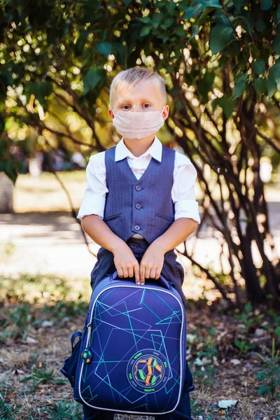 Coronavirus and new rules for staying at school. An elementary school student goes to school in the morning. Always wear a protective medical mask. Looks smart and neat in a new uniform. Covid-19.