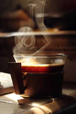 Masada sigara dumanı olan küçük cam bir fincan sade kahve. Koyu arkaplan. 