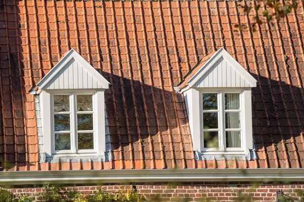 On a red roof there are two dormer windows with wood windows