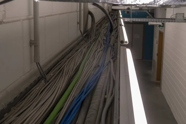 In the corridor of a large building, electrical cables hang from the ceiling in a cable duct