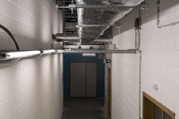 In the corridor of a large building, electrical cables hang from the ceiling in a cable duct