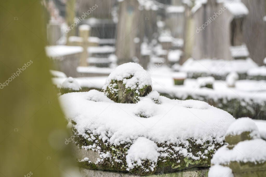 In a cemetery or cemetery, there is a skull with moss on a gravestone and its covered whit snow.