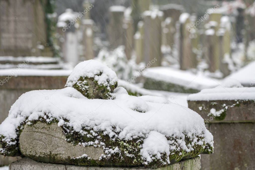In a cemetery or cemetery, there is a skull with moss on a gravestone and its covered whit snow.