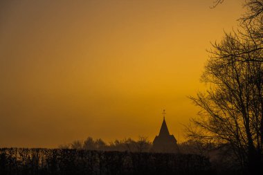 Sisli bir sabah, bu kilise kulesi sabah ışığında ağaçların yanında.
