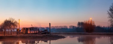 Nehir boyunca sisli, soğuk bir sabahta güzel bir teknenin demirlediği yerde