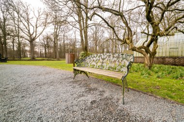 Parkta yaprak motifli antika bir bank var.