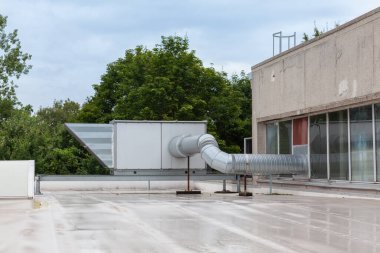 Endüstriyel bölgedeki yüksek bir binanın çatısında vantilatörler var.