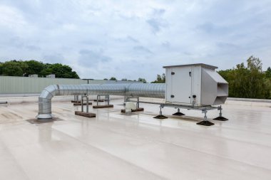 Endüstriyel bölgedeki yüksek bir binanın çatısında vantilatörler var.