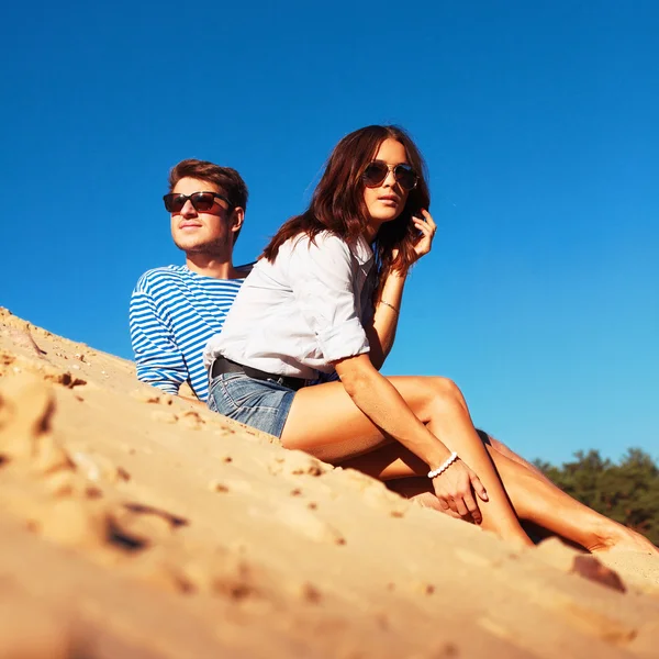 Fashion couple sitting on sand — Stock Photo, Image