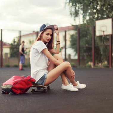 girl sitting on skateboard with backpack