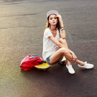 girl sitting on skateboard with backpack