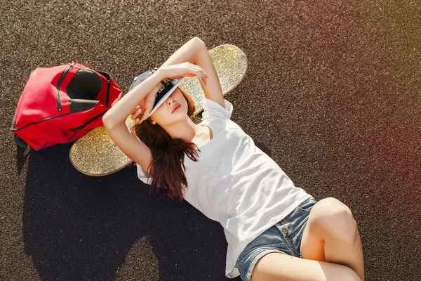 Женщина лежит на земле со скейтбордом и рюкзаком — стоковое фото