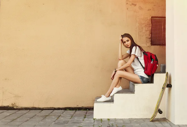 Girl with skateboard and backpack sitting on the stairs — Stock fotografie