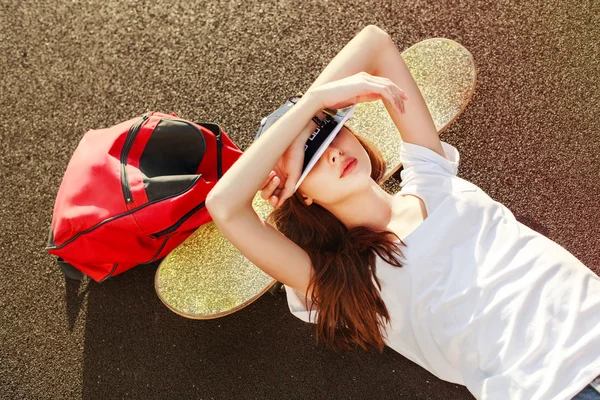 Woman  lying on the ground with skateboard and backpack — Stockfoto