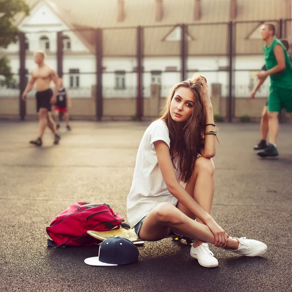 Девушка сидит на скейтборде с рюкзаком — стоковое фото