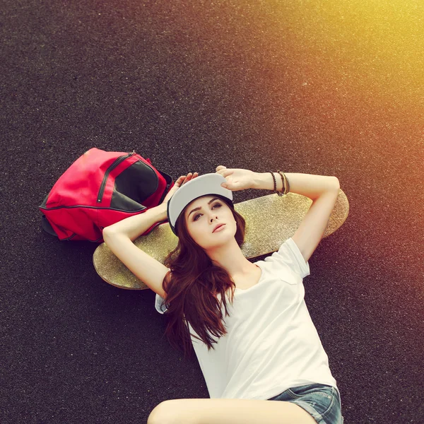 Mujer acostada en el suelo con monopatín y mochila — Foto de Stock