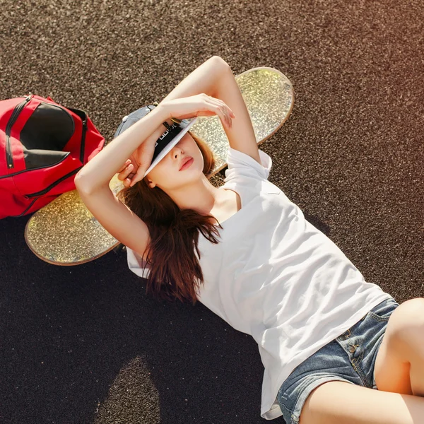 Mulher deitada no chão com skate e mochila — Fotografia de Stock