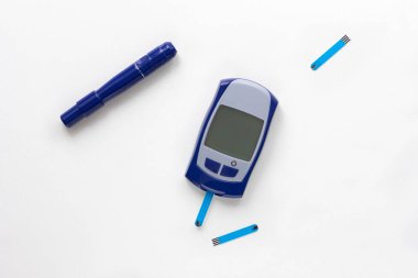 Beyaz zemin üzerinde kan glikoz ölçer, neşter ve test şeridi üst görünümü