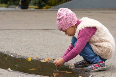 Beş yaşındaki beyaz çocuk sonbahar parkında su birikintisinden suyla oynuyor.