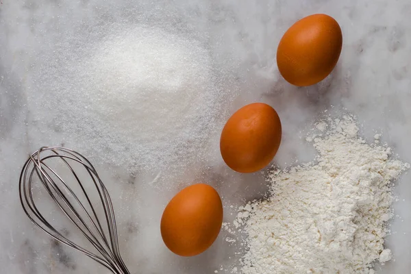 Вид сверху коричневых яиц, сахара, муки в качестве ингредиентов и венчиком на мраморном фоне — стоковое фото