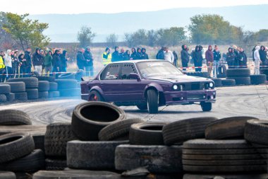 Bulgaristan 'ın Buhovtsi kenti - 12.10.2025 - Mor bir araba, bir motor sporu etkinliğinde lastik bariyerlerinin etrafında sürükleniyor. İzleyiciler pist etrafında toplanmış, gündüz etkinliklerinin tadını çıkarıyorlar..