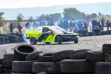 Buhovtsi, Bulgaristan - 12.10.2025 - Parlak yeşil bir drift araba yarış pistinde heyecan verici manevralar yaparken lastiklerden duman yükseliyor. Heyecanlı izleyiciler belli bir mesafeden izleyip, canlı bir atmosfer yaratıyorlar..