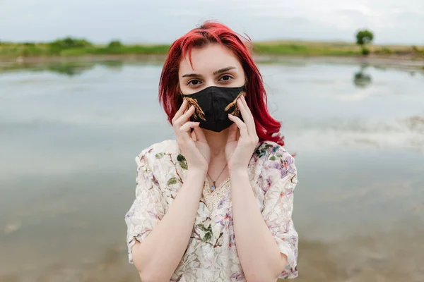 Corona fashion. Red hair girl wearing creative medical mask and holding it with two hands