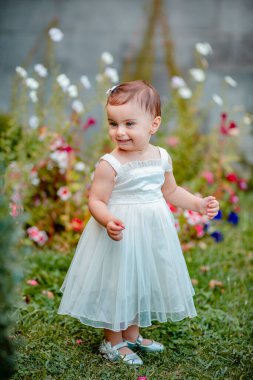 Bahçedeki çimlerin üzerinde duran ve gülümseyen uzun beyaz elbiseli neşeli kız.